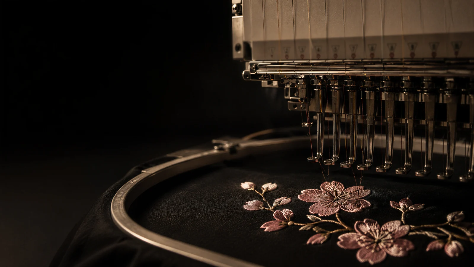 A Hoodify embroidery machine mid-run, stitching a cherry blossom design into black fabric held in the hoop
