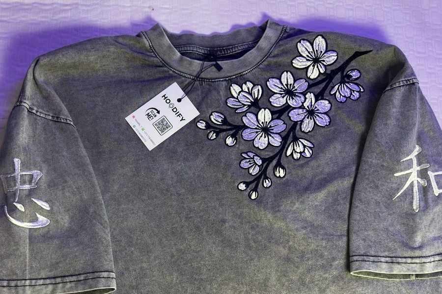 Stonewashed grey t-shirt laid flat, embroidered with a cherry blossom branch over one shoulder and a Japanese character on each sleeve